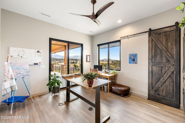 home office featuring a barn door, ceiling fan, and light hardwood / wood-style floors