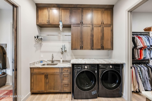 washroom featuring washing machine and dryer, sink, cabinets, and light hardwood / wood-style flooring