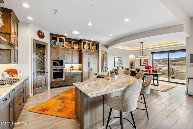 kitchen featuring appliances with stainless steel finishes, light wood-type flooring, light stone counters, sink, and a large island with sink