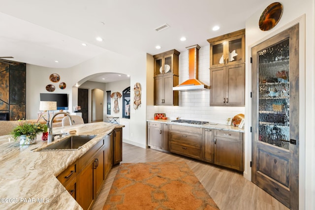 kitchen with backsplash, light stone countertops, wall chimney range hood, and sink