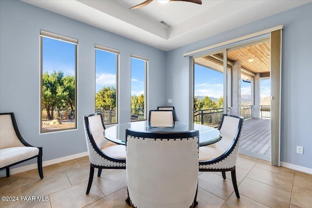 tiled dining room with ceiling fan and a tray ceiling