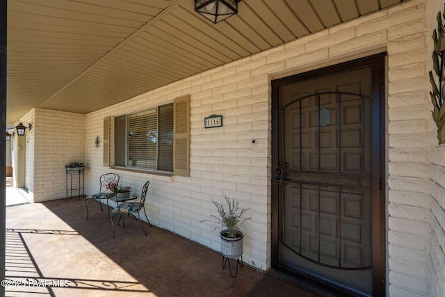 view of exterior entry featuring brick siding and a porch