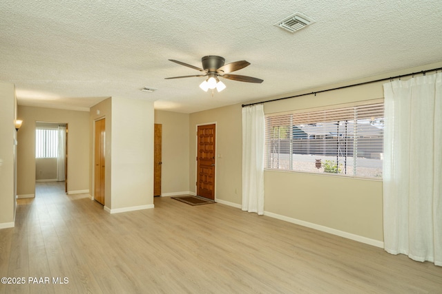 empty room with light wood-style floors, visible vents, a wealth of natural light, and ceiling fan