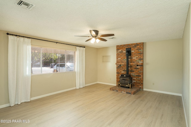 unfurnished living room with a textured ceiling, visible vents, light wood-style floors, ceiling fan, and a wood stove