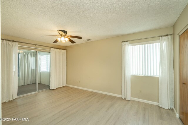 unfurnished bedroom featuring baseboards, light wood finished floors, a textured ceiling, and visible vents