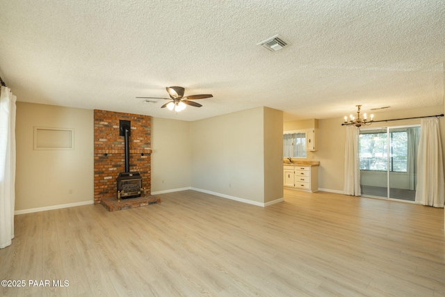 unfurnished living room with a textured ceiling, visible vents, light wood-style floors, ceiling fan with notable chandelier, and a wood stove