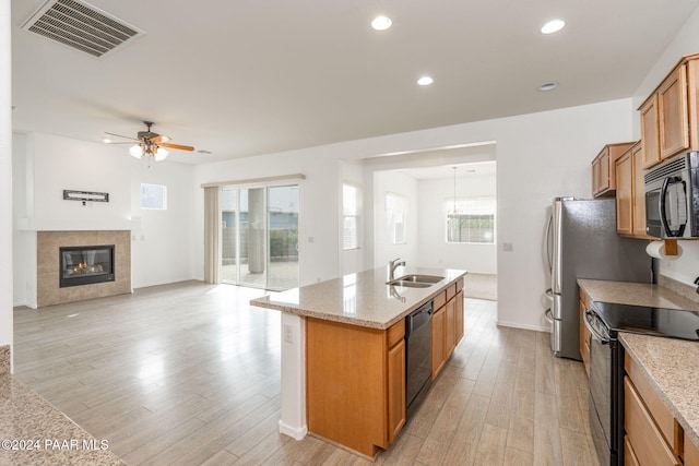 kitchen featuring sink, black dishwasher, stainless steel electric stove, a kitchen island with sink, and light wood-type flooring