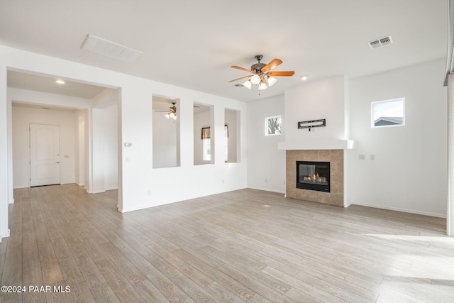 unfurnished living room with ceiling fan, light wood-type flooring, and a tiled fireplace