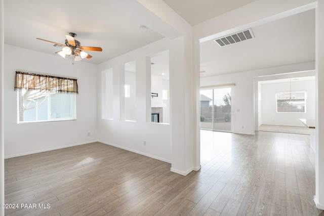 empty room with a healthy amount of sunlight, ceiling fan with notable chandelier, and light wood-type flooring