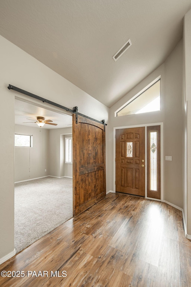 entrance foyer featuring visible vents, wood finished floors, baseboards, a barn door, and lofted ceiling