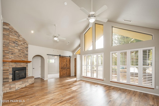 unfurnished living room featuring visible vents, high vaulted ceiling, a ceiling fan, wood finished floors, and a barn door