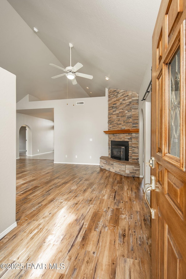 unfurnished living room with hardwood / wood-style floors, a ceiling fan, lofted ceiling, arched walkways, and a stone fireplace