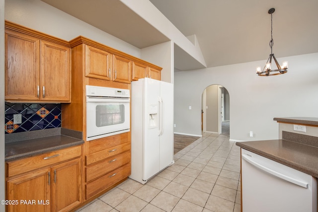 kitchen featuring dark countertops, tasteful backsplash, white appliances, arched walkways, and light tile patterned flooring