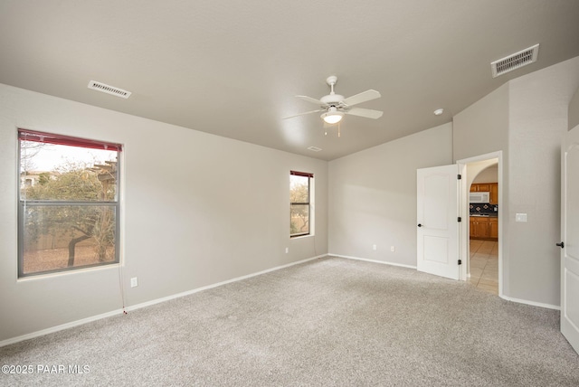 empty room with lofted ceiling, light colored carpet, visible vents, and ceiling fan