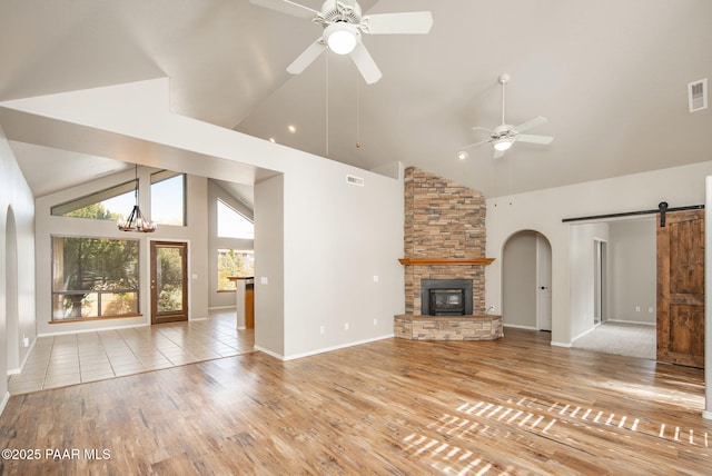 unfurnished living room featuring visible vents, ceiling fan with notable chandelier, light wood-style floors, and a barn door