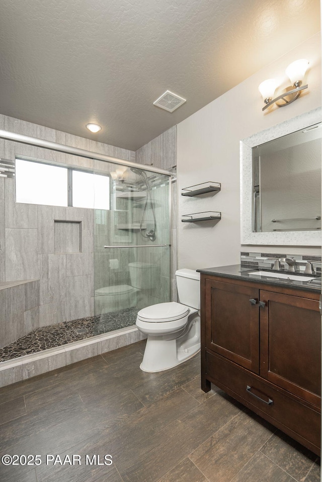 full bathroom featuring toilet, a stall shower, wood finished floors, a textured ceiling, and vanity