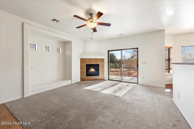 unfurnished living room with a tiled fireplace, ceiling fan, plenty of natural light, and carpet