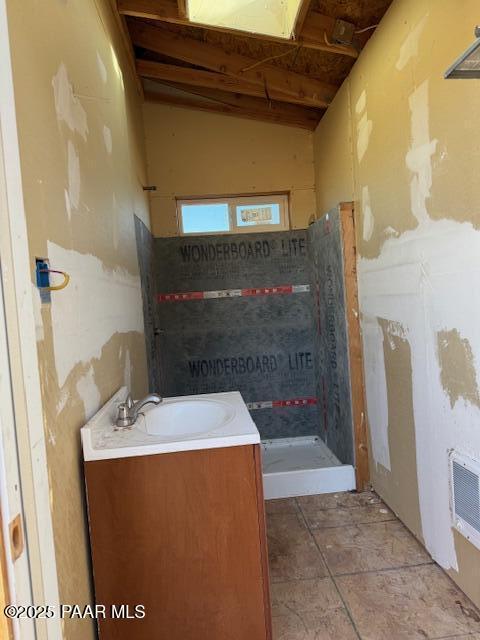 bathroom with a tile shower, vanity, and lofted ceiling