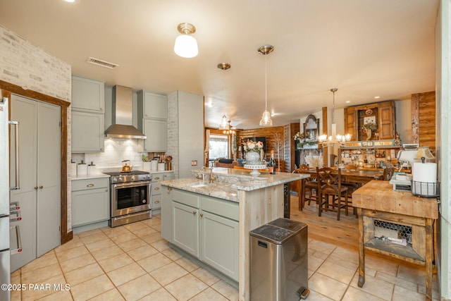 kitchen featuring hanging light fixtures, light stone counters, high end stove, a kitchen island, and wall chimney exhaust hood