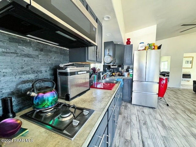 kitchen featuring decorative backsplash, stainless steel fridge, gas stovetop, light wood-type flooring, and ceiling fan