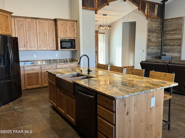 kitchen featuring sink, stone counters, a kitchen breakfast bar, black appliances, and a center island with sink