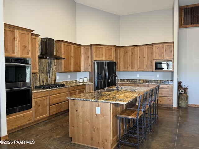 kitchen featuring sink, a high ceiling, black appliances, a center island with sink, and wall chimney exhaust hood