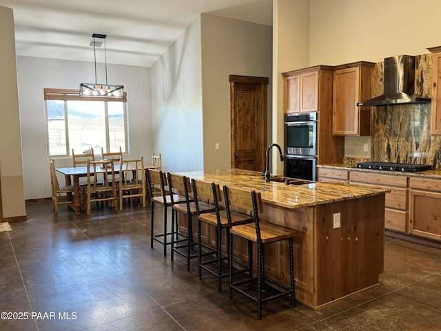 kitchen featuring a kitchen island with sink, wall chimney range hood, hanging light fixtures, and sink