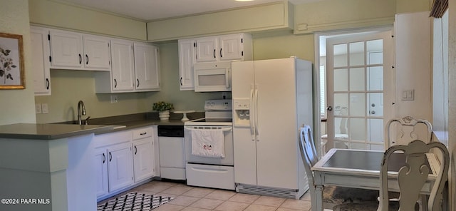 kitchen with dark countertops, white cabinets, a sink, light tile patterned flooring, and white appliances