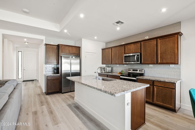 kitchen with a center island with sink, sink, light hardwood / wood-style flooring, light stone counters, and stainless steel appliances