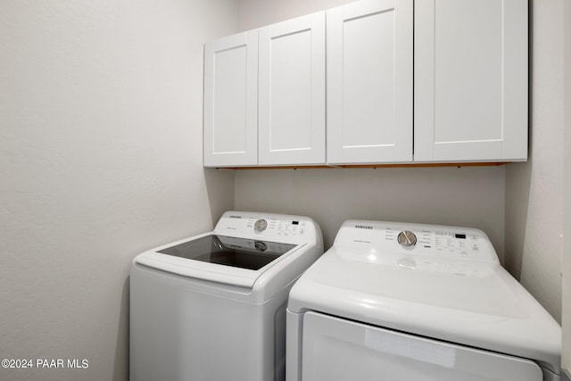 clothes washing area featuring separate washer and dryer and cabinets