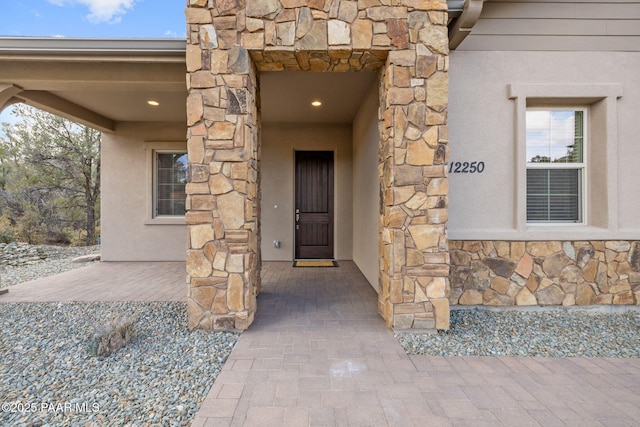 view of exterior entry featuring stone siding and stucco siding