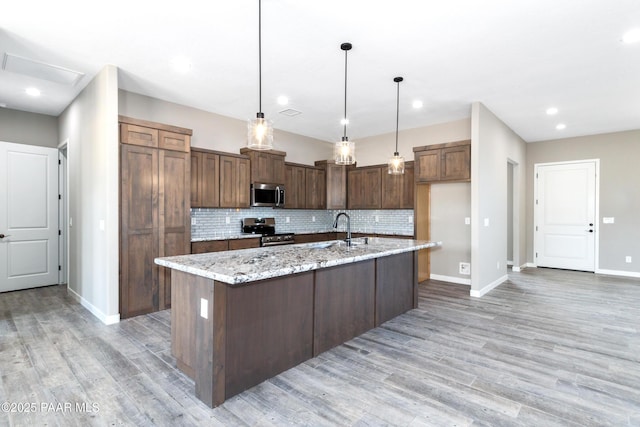 kitchen featuring light stone counters, stainless steel appliances, tasteful backsplash, light wood-style floors, and an island with sink