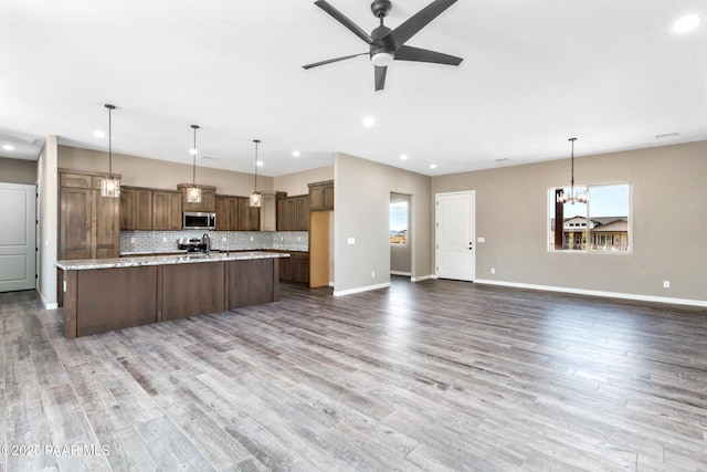 kitchen featuring stainless steel appliances, tasteful backsplash, wood finished floors, baseboards, and ceiling fan with notable chandelier