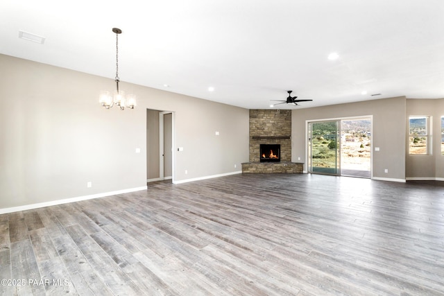 unfurnished living room featuring ceiling fan with notable chandelier, a fireplace, baseboards, and wood finished floors