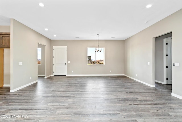 unfurnished living room featuring an inviting chandelier, baseboards, wood finished floors, and recessed lighting