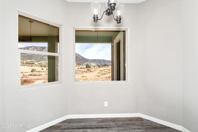 spare room with an inviting chandelier, a mountain view, baseboards, and dark wood finished floors