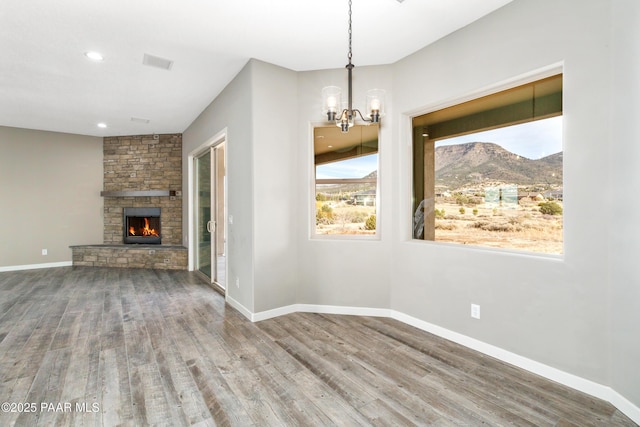 unfurnished dining area featuring a stone fireplace, a mountain view, a chandelier, and hardwood / wood-style flooring