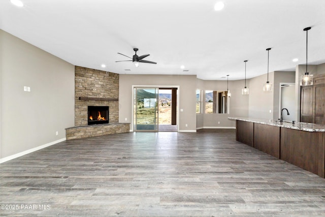 unfurnished living room featuring a sink, a stone fireplace, baseboards, and wood finished floors