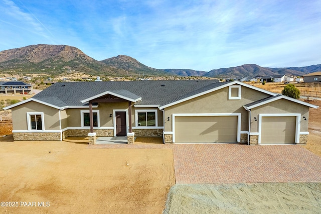 craftsman inspired home with a garage, stone siding, decorative driveway, a mountain view, and stucco siding