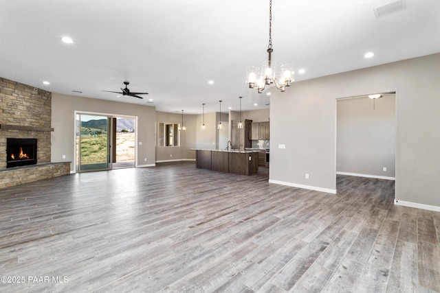 unfurnished living room featuring hardwood / wood-style floors, ceiling fan with notable chandelier, and a stone fireplace