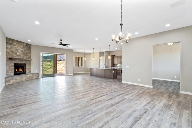 unfurnished living room with a fireplace, visible vents, a sink, wood finished floors, and ceiling fan with notable chandelier