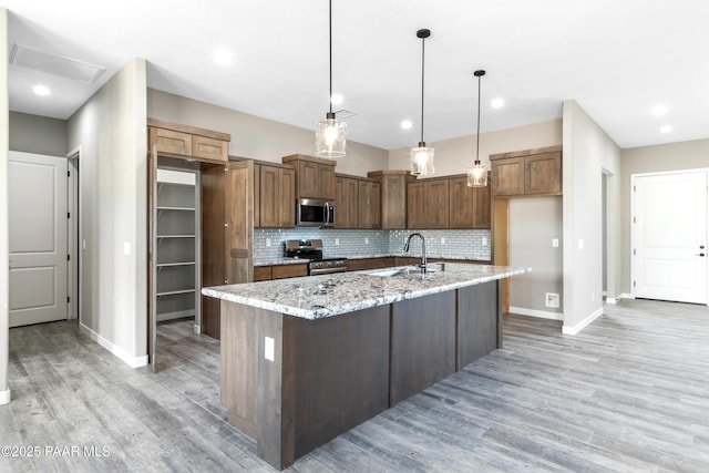 kitchen with stainless steel appliances, decorative backsplash, light wood-style floors, a sink, and light stone countertops