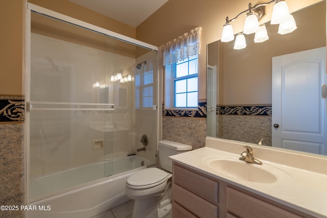 full bathroom featuring tile walls, vanity, toilet, a wainscoted wall, and combined bath / shower with glass door