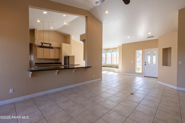 kitchen with light tile patterned floors, a breakfast bar, baseboards, light brown cabinetry, and vaulted ceiling