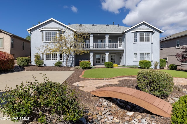 view of front of property featuring stucco siding, a balcony, french doors, and a front lawn