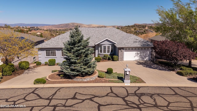 ranch-style home featuring roof with shingles, concrete driveway, a mountain view, and an attached garage