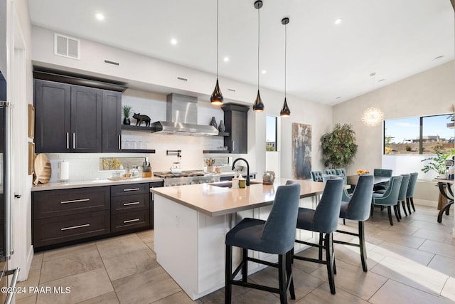 kitchen featuring tasteful backsplash, a breakfast bar, sink, wall chimney range hood, and decorative light fixtures