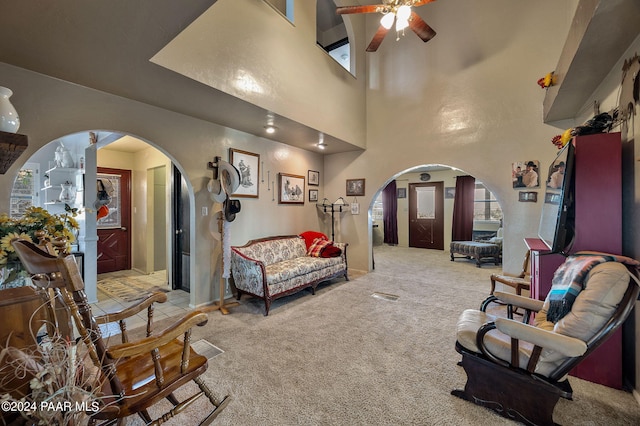 living room featuring plenty of natural light, ceiling fan, light colored carpet, and a high ceiling