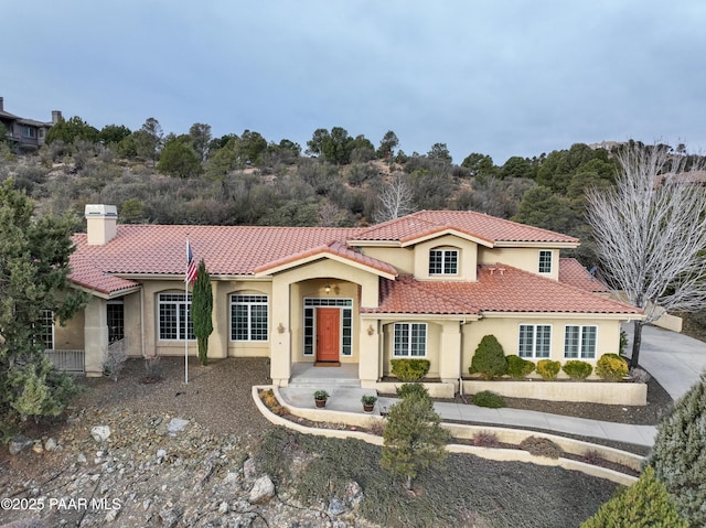 mediterranean / spanish home featuring a tiled roof, a chimney, and stucco siding