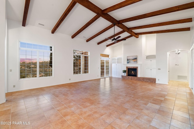 unfurnished living room with a ceiling fan, visible vents, high vaulted ceiling, a glass covered fireplace, and beamed ceiling